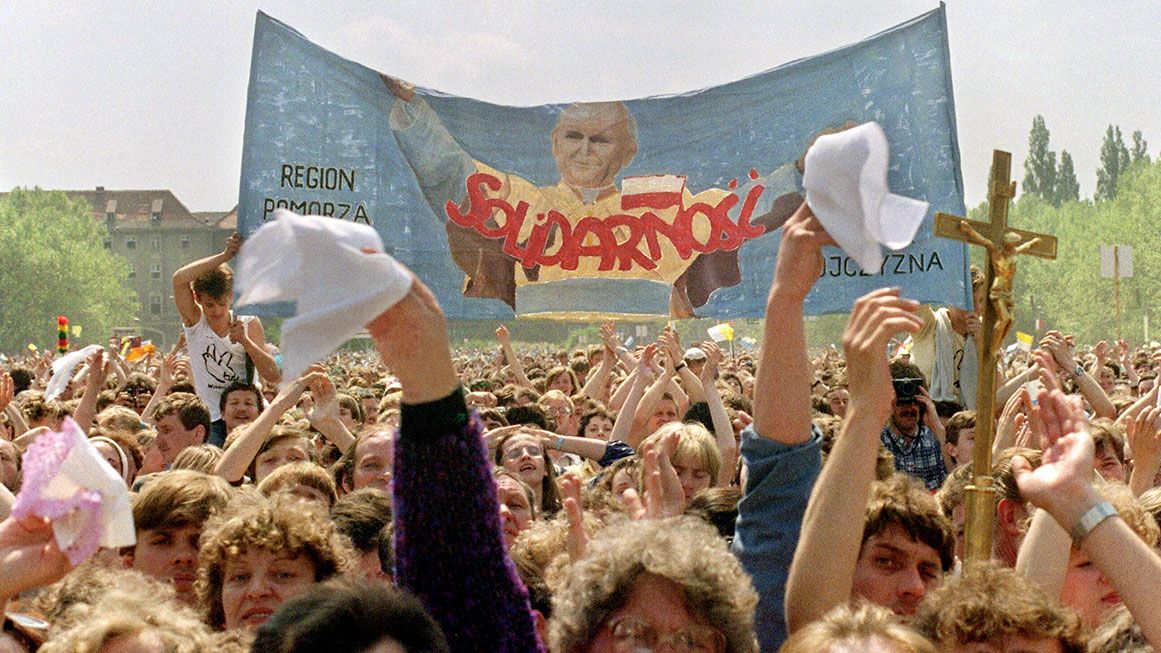 slade | Photo: Supporters of the outlawed Solidarity trade union wave a banner during the pope’s 1987 trip to Poland. Marcel Mochet/AFP/Getty
