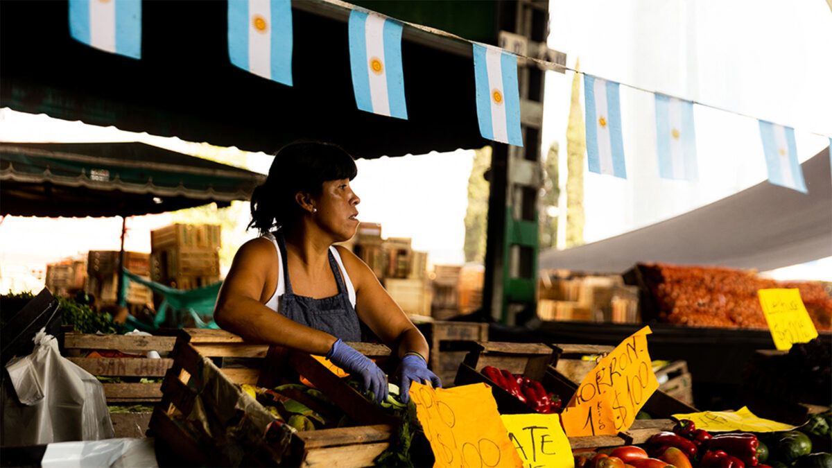 A woman standing at a produce stand beneath a banner of Argentine flags |  Tomas Cuesta/Getty
