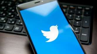 Image of a Twitter logo on a smartphone, which is sitting on a laptop keyboard.