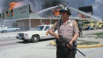 book1 | A Dade County policeman stands guard as firemen battle a blaze during the third day of racial violence; Bettmann/Getty