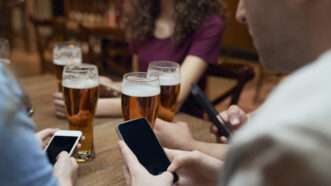 friends drinking a beer at a restaurant while on their phones | gpointstudio/Westend61 GmbH/Newscom