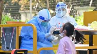 a person wearing personal performs a nasal swab on a young girl protective equipment