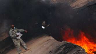 A man in a military uniform stands near a burn pit