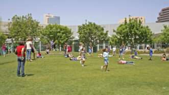 Elementary school students running around a park under a blue sky. | Mark Gibson / Danita Delimont Photography/Newscom