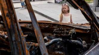 Little girl looking through empty windshield of burned out car in Ukraine.