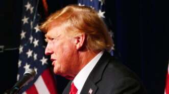 Photo of the side of Donald Trump's head as he speaks into a microphone with American flags behind him. | MEGA / Newscom/BPLAS2/Newscom
