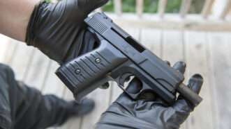 Gun being held on a deck by black gloved hands | Shane T. McCoy/U.S. Marshals/Flickr