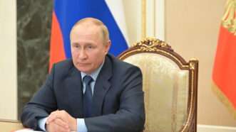 Russian President Vladimir Putin sitting at a table with notes in front of him