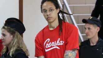 Brittney Griner, in a red t-shirt and handcuffs