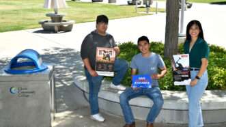 Three students stand in the campus of Clovis Community College, holding anti-communist posters