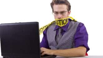 Man with yellow tape wrapped around his mouth while on a laptop