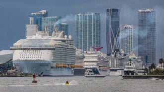 Cruise ships at a U.S. port. Smoke blows from the ships. A skyline is visible in the background | Al Diaz/TNS/Newscom