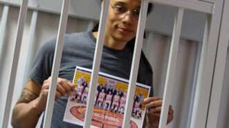Britteny Griner behind bars, holding a photo of her basketball teammates.
