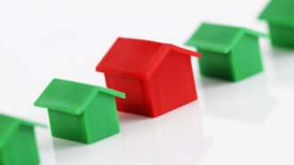 a row of little green plastic houses with a larger red plastic house in the middle on a white background