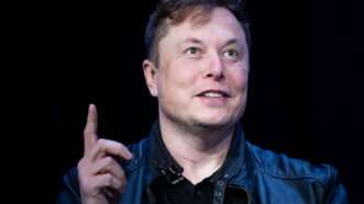 A photo of Elon Musk pointing to the ceiling against a black background | BRENDAN SMIALOWSKI / GDA Photo Service/Newscom