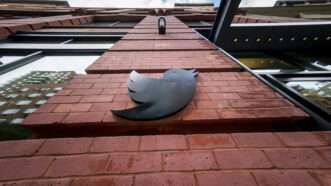 black Twitter logo affixed to a brick building in a vertical shot