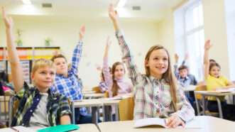 Students in a classroom raising their hands.