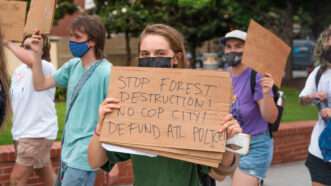 A masked protester holds up a sign saying "Stop forest destruction! No Cop City! Defund ATL police!" | Andrew Clark/ZUMAPRESS/Newscom