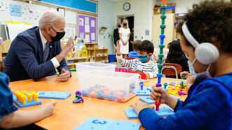 A masked Joe Biden talks to children in a classroom