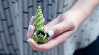 woman's hand holding glass bowl with marijuana in it