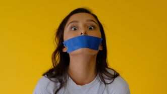 A young woman with blue tape over her mouth against a yellow background | Photo by Brian Wangenheim on Unsplash