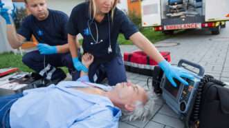 Paramedics, crouched, attend to an unconscious man who is flat on his back. | Candybox Images | Dreamstime.com