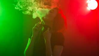 Woman smoking an e-cigarette in front of neon lights | Photo 122603552 © Tatiana Chekryzhova | Dreamstime.com
