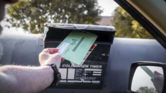 A hand extends from a car and places a ballot in a mail box. | Photo 198056143 © Susan Vineyard | Dreamstime.com
