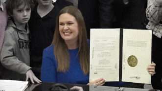 Arkansas Gov. Sarah Huckabee Sanders holds up a copy of the Youth Hiring Act after signing it into law. | Illustration: Lex Villena; ABC 40/29 News (YouTube)