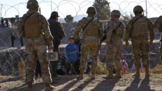 Members of the Texas National Guard and Texas Department of Public Safety speak to asylum seekers at the U.S.-Mexico border in El Paso