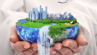 a model of the world with a city and a waterfall and a plane flying above it is held in the hands of someone seeming to wear religious robes | Igor Zakharevich | Dreamstime.com