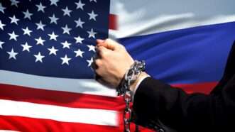 A side-by-side of the U.S. and Russian flags, with a person's handcuffed hands in the foreground | America Russia © motortion | Dreamstime.com