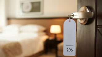 The entrance to a hotel room, with a keytag reading "206" hanging on the doorknob in the foreground and the room itself blurry in the background. | Dragonimages | Dreamstime.com