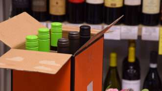 Box of wine bottles in front of a shelf with wine | Photo 209204568 © Martins Pormanis | Dreamstime.com