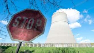A stop sign in the foreground, with a smokestack of the Emsland nuclear power plant in Lower Saxony, Germany, in the background.