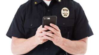 A faceless police officer uses a smartphone. | Seanlockephotography | Dreamstime.com