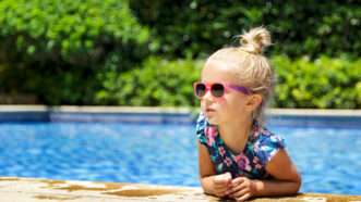 Little girl wearing sunglasses leans against side of the pool