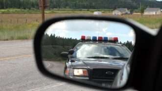 A pulled over car shows a police cruiser behind it in the side mirror