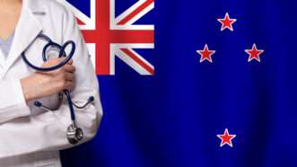A close-up of a doctor with a stethoscope against a backdrop of the New Zealand flag. | Millafedotova | Dreamstime.com