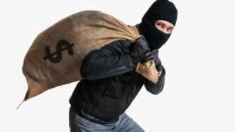 A masked man hauls away a burlap bag with a dollar symbol on it on a white background