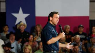 Ron DeSantis speaks in front of a large Texas flag at an event