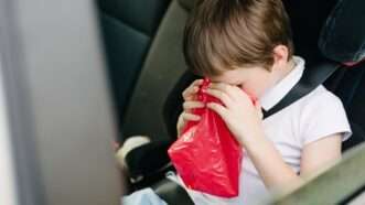 Child in the backseat with his face in a barf bag. | Djedzura | Dreamstime.com