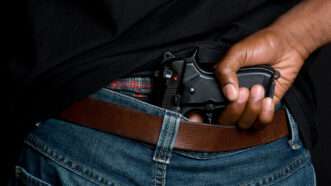 A man holds a gun in his rear wasteband. | Jason Stitt | Dreamstime.com