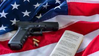 A handgun and a copy of the Constitution against a backdrop of the American flag. | Olga Mendenhall | Dreamstime.com