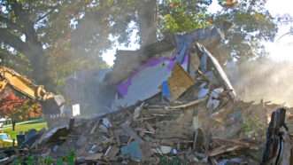 A backhoe finishes demolishing a house. | Evaulphoto | Dreamstime.com