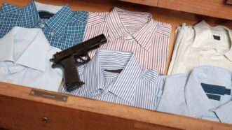 A handgun sits atop a row of folded shirts in a dresser drawer. | Tommaso79 | Dreamstime.com