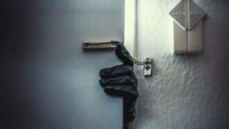 A gloved hand reaches through a cracked door that still has the deadbolt on. | Audioundwerbung | Dreamstime.com