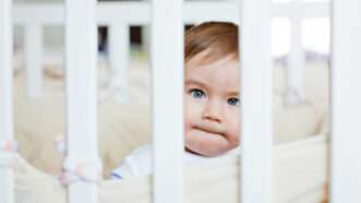 A baby boy's face seen through the slats of his crib, giving an effect of prison bars. | Maria Butrova | Dreamstime.com