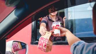 A McDonalds' drive-through worker hands a customer their food out the window | Photo 92599281 | American © Punporn Aphaithong | Dreamstime.com