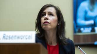 FCC Chairwoman Jessica Rosenworcel sits in a congressional hearing room behind a placard bearing her name, wearing a navy blazer and a red shirt and holding a mechanical pencil. | om Williams/CQ Roll Call/Newscom